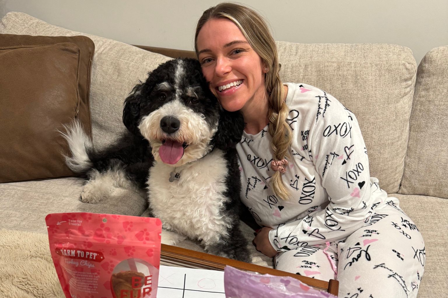 Woman in pajamas sitting on a couch cuddling with her dog